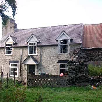 Two storey slate house with 3 dormers and attached barn with corrugated metal roof.