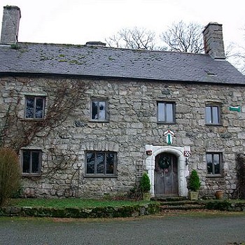 Large stone house with slate roof and chimney at each gable.